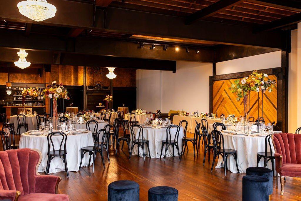 The ballroom set for a reception: round tables in white linen, tall floral arrangements, chandeliers and the herringbone wood wall